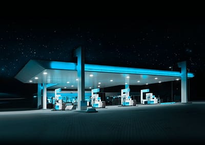A wide-angle photo of a service station at night, rendered in blue and black tones