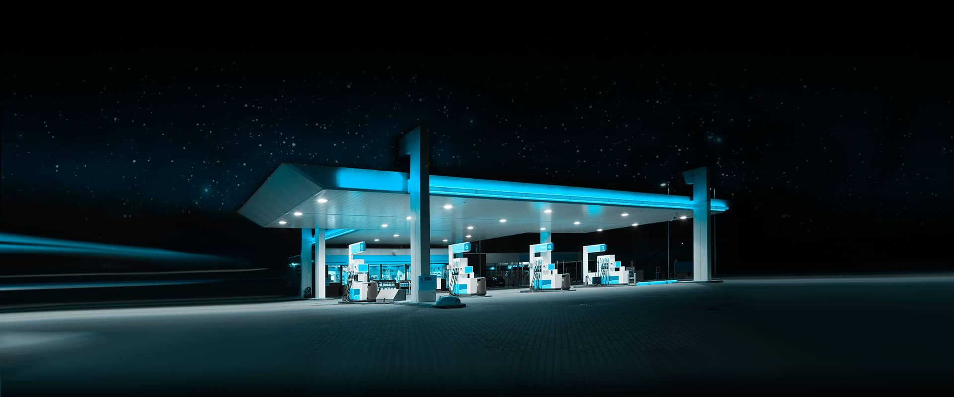 A wide-angle photo of a service station at night, rendered in blue and black tones